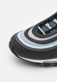 Sportskor med en design i svart, grått och ljusblått, med en texturerad mesh-övre del, lager på lager-mönster och kontrasterande snören.