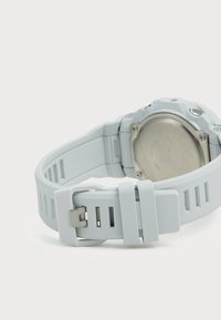 Bracelet de montre en silicone bleu clair avec un design découpé, dos en acier inoxydable et fermoir ajustable. Présente une surface texturée.