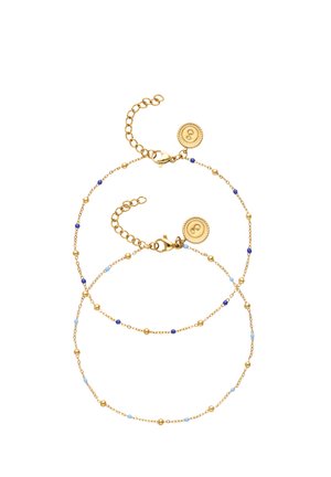 Dos delicadas pulseras de cadena dorada con pequeñas cuentas azules y doradas, cada una con una etiqueta redonda de cierre dorado con un símbolo grabado.