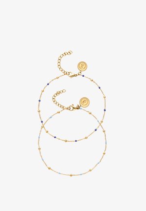 Deux bracelets délicats en chaîne d'or avec de petites perles bleues et dorées, chacun doté d'une étiquette ronde en or avec un symbole gravé.