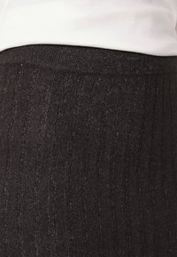 Tessuto a costine nero con una consistenza morbida, dotato di una cintura elastica ampia. Il materiale appare leggermente lucido alla luce.