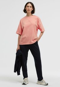Helles rosa, oversized Baumwoll-T-Shirt mit kurzen Ärmeln, rundem Halsausschnitt und Logodetail; kombiniert mit marineblauen Hosen und silbernen Sneakers.
