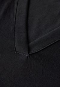 Schwarzer Stoff mit glatter Textur, mit umgeschlagenem Kragen und sichtbaren Nähten. Nahaufnahme eines Hemd- oder Oberteil-Designs.