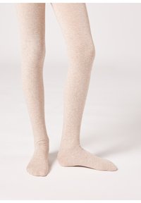 Jasno beżowe rajstopy wykonane z miękkiego, teksturowanego materiału. Posiadają gładkie wykończenie i dopasowany krój, zakrywający nogi aż do palców.