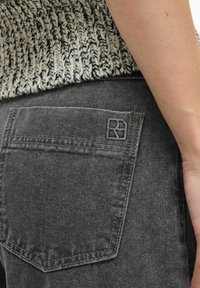 Grå denimjeans med en bakficka som har en diskret logotyp, som visar en slät textur och rena sömnadsdetaljer.