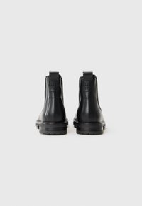 Botas de cuero negro hasta el tobillo con suelas planas, tiradores y un diseño de costuras mínimas. Presentan una textura suave y una punta redondeada.