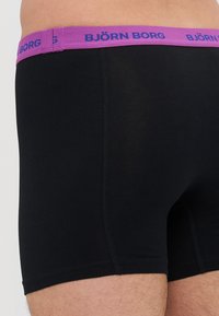 Boxers noirs en tissu lisse, avec une ceinture violette arborant le logo "BJÖRN BORG" en bleu. Aucun motif ou accent visible.