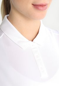 Polo bianco con colletto classico, dotato di una pattina con tre bottoni, morbida al tatto e dalla finitura liscia.