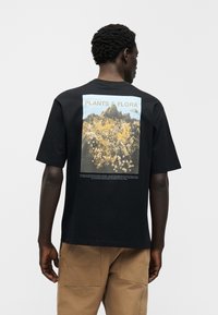 Μαύρο βαμβακερό T-shirt με κοντά μανίκια, με γραφική εκτύπωση της κοιλάδας του Yosemite στην πλάτη, με λεπτομέρειες φυτών και λουλουδιών.