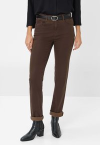 Pantaloni marroni in cotone, con taglio slim, risvolti e tasche frontali. Indossati con una cintura nera e stivaletti.