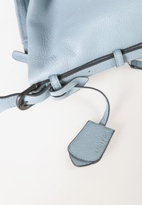 Helleblauer Leder-Rucksack mit strukturiertem Leder, ausgestattet mit schwarzen Akzenten und einem Clipverschluss. Enthält ein markiertes Lederlabel.