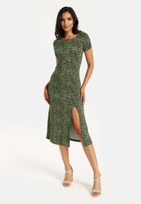 Green leopard-print dress with short sleeves, fitted silhouette, and side slit; paired with matching strappy high-heeled sandals.