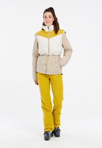 Beige ir baltas džemperis su geltonu pečių užsegimu, turi reguliuojamą liemeni. Suderintas su ryškiai geltonomis kelnėmis.