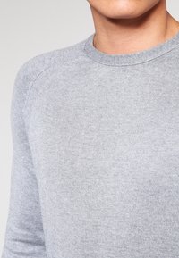 Pull gris côtelé avec un col rond et des manches longues, fabriqué dans un tissu doux et texturé avec des coutures minimalement visibles.