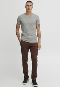Siva majica s V-izrezom, uparena s smešnim hlačama i crnim patikama, sa slim fit krojem i kratkim rukavima, na neutralnoj pozadini.
