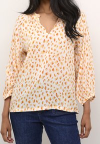Blouse légère de couleur pêche avec un col en V et des manches trois-quarts. Elle présente un motif épars orange et rose, des poignets élastiques et une coupe décontractée.