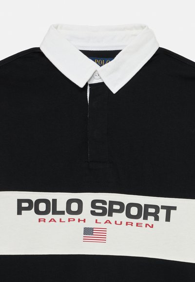 Camisa polo preta com colarinho branco, apresentando um grande gráfico "POLO SPORT" e uma bandeira americana no peito. Material em algodão.