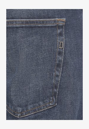 Tasca posteriore di jeans in denim con cuciture arancioni e una piccola lettera metallica "D" attaccata alla cucitura laterale destra della tasca.