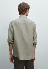 Camicia verde chiaro a maniche lunghe con vestibilità rilassata, righe verticali e polsini con bottoni. Tessuto morbido con una consistenza liscia.