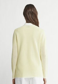 Pull en maille jaune avec manches longues et un col discret. Caractérisé par un tissage ouvert pour une meilleure respirabilité et une coupe décontractée.