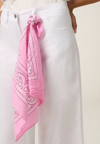 Pantalon blanc avec despoches avant et un bandana paisley rose noué à travers une boucle de ceinture sur le côté droit.