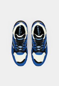 Μπλε και λευκά αθλητικά παπούτσια με υφασμένο επάνω μέρος, μαύρες λεπτομέρειες και σχεδιαστικό μοτίβο. Διαθέτουν μαύρα κορδόνια και μαλακή σόλα.
