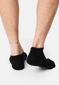 Schwarze Knöchelsocken aus Stoff mit geripptem Bündchen und strukturiertem Sohle für besseren Halt. Sichtbarkeit der Füße und Unterschenkel dargestellt.