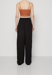 Black wide-leg pants with a relaxed fit, paired with an orange crop top featuring a wavy pattern and thin shoulder straps.