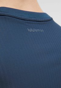 Camiseta deportiva azul marino con cuello acanalado y logo "lululemon" en relieve en la parte posterior para branding. Fabricada con un material suave y ligero.