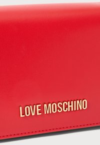 Punane kunstnahast rahakott, millel on tekstureeritud pind, kuldne "LOVE MOSCHINO" logo ja korralik õmblus servade ümber.