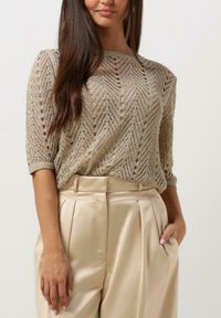 Pull en maille beige clair avec un motif en chevrons et des manches trois-quarts, associé à un pantalon plissé de couleur crème à taille haute.