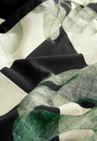 Tissu avec des motifs de feuilles abstraites en noir, beige et vert, montrant une texture et des plis doux.