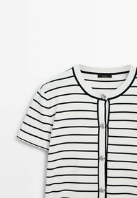 Cardigan blanc à manches courtes avec des rayures horizontales noires et des boutons à l'avant, avec un col rond et une bordure en côtes.