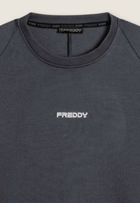 Maglietta grigia scura a girocollo con logo bianco "FREDDY" centrato sul petto e etichetta corrispondente all'interno del colletto.
