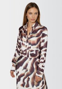 Satin button-up shirt with a fluid shape, featuring a brown and white abstract pattern, long sleeves, and contrasting button accents.