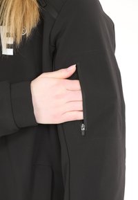 Haut de sweatshirt zippé noir avec une poche zippée sur le haut du bras, texture de tissu lisse et texte graphique blanc sur la poitrine.