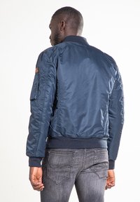Veste bomber bleu marine avec fermeture éclair, poches latérales, poignets et ceinture côtelés, confectionnée dans un matériau lisse et léger.
