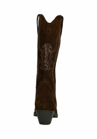 Botte de cowboy en daim marron avec un bout pointu, des coutures décoratives et un petit talon. Présente des découpes sur la tige.