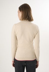 Maglione beige con colletto alto e maniche lunghe. Polsini e orlo a coste con una sottile accentuazione rossa. Texture morbida, design aderente.