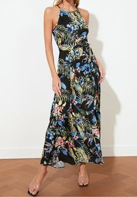 Květinové maxi šaty v černé barvě s tropickými vzory v zelené, modré a růžové. Design s halter krkem, stáhnutý pas a splývavá látka.