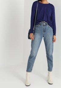 Granatowa bluzka z długim rękawem połączona z jasnoniebieskimi, wysokim stanem dżinsami oraz białymi botkami za kostkę. Torebka to czarna skóra z paskiem.