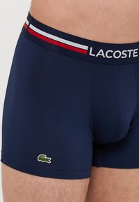 Boxers en coton stretch bleu avec une ceinture à logo Lacoste multicolore et un petit logo de crocodile vert en bas à gauche.