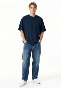 Mornarsko modra oversize majica, mešanica bombaža, okrogla izrezana. Svetlo modri ravni jeans z bledejšimi akcenti. Bele superge. Preprost dizajn.