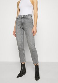 Jeans de tiro alto y pierna recta en denim gris claro, con dobladillo deshilachado y un leve desvanecimiento, combinados con botas negras hasta el tobillo.