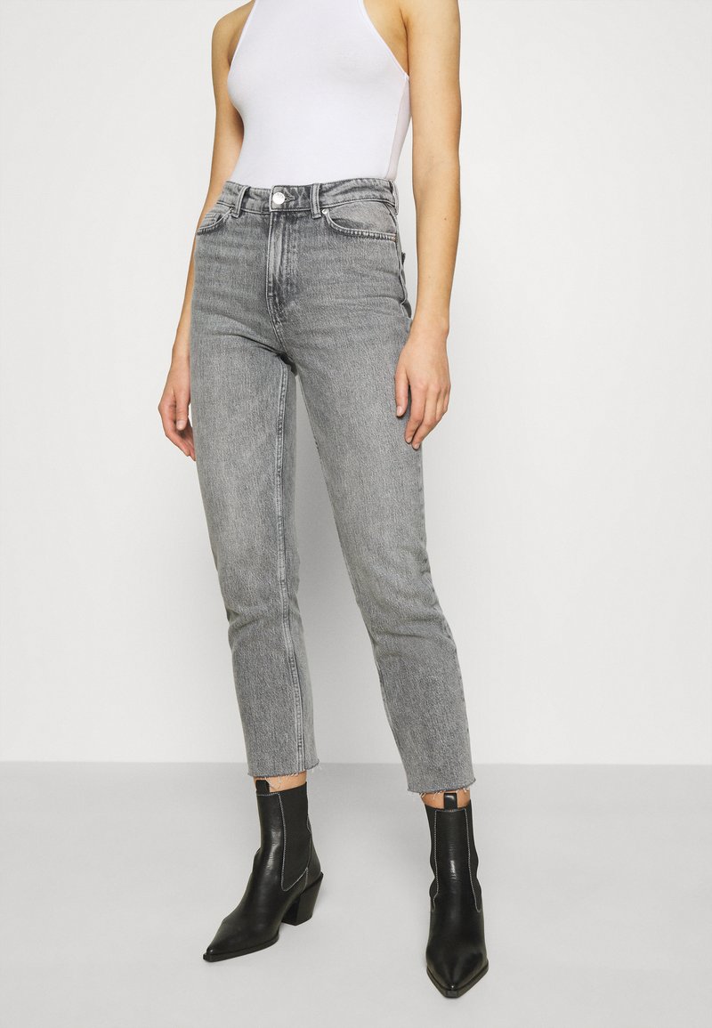 Jeans de tiro alto y pierna recta en denim gris claro, con dobladillo deshilachado y un leve desvanecimiento, combinados con botas negras hasta el tobillo.