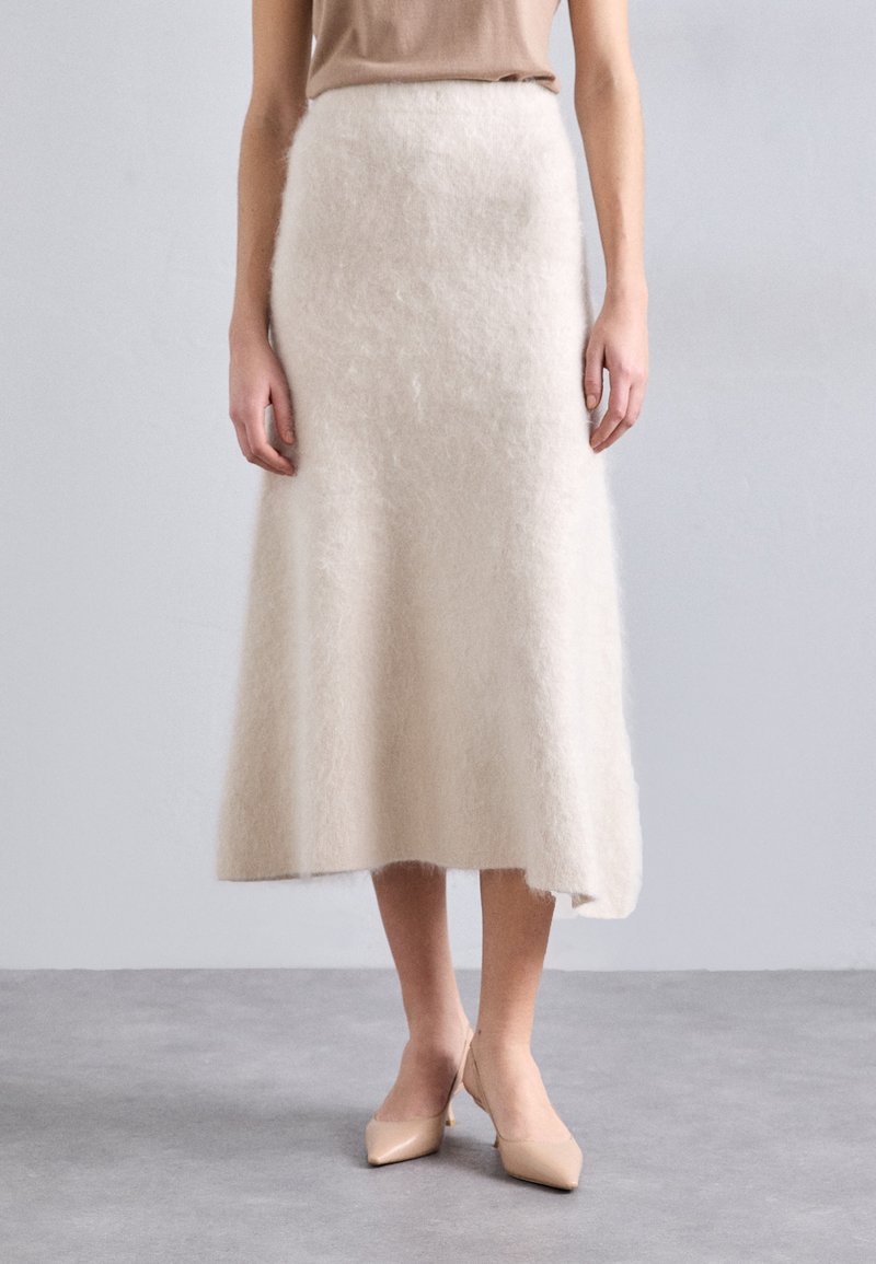 Cremefarvet midi-nederdel lavet af blødt, fluffy stof; A-formet silhuet med en glat tekstur. Båret med lyse nude højhælede sko.