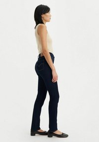 Blå denim skinny jeans med hög midja, diskret sömnad och en märkesläderlapp på baksidan. Bärs med en beige linne och svarta ballerinaskor.