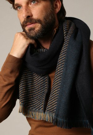 Écharpe tissée en bleu marine et bleu avec un motif à carreaux, dotée de bords à franges et d'une texture douce. Design chaud et oversize.