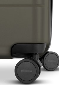 Harde koffer in donkergroen met een gestructureerd oppervlak. Voorzien van vier zwarte wielen met "ETERNITIV3"-merk en een beschermende basis.