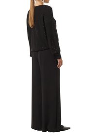 Schwarzer Strickpullover mit lockerer Passform, verziert mit dekorativen Löchern und langen Ärmeln, kombiniert mit weit geschnittenen schwarzen Hosen.